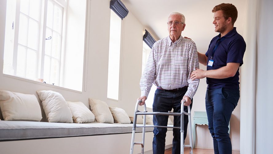 Verzorger helpt oude man met wandelrekje in zorgtehuis