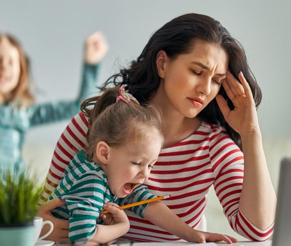 Stress bij het thuiswerken: vrouw probeert op haar laptop te werken terwijl haar twee kinderen aandacht opeisen
