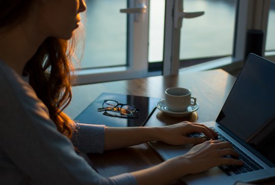 Jonge vrouw werkt op laptop naast een open raam