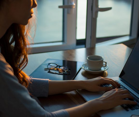 Jonge vrouw werkt op laptop naast een open raam