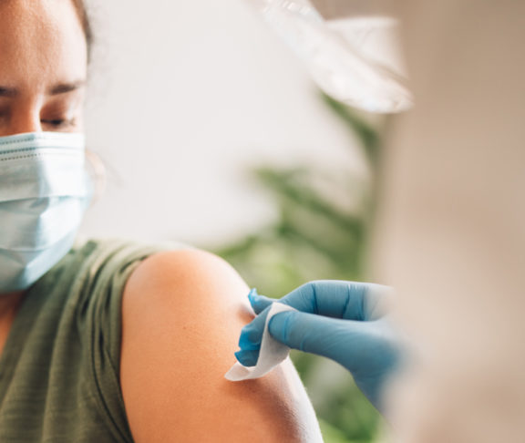 Woman getting vaccine at home. Healthcare professional cleaning and disinfecting female's arm before giving coronavirus vaccination shot at home.