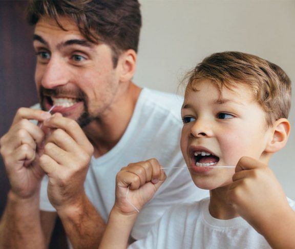 Father and son flossing their teeth in front of a mirror