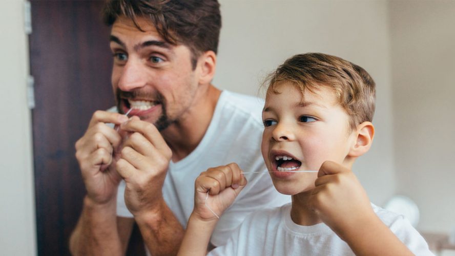 Father and son flossing their teeth in front of a mirror