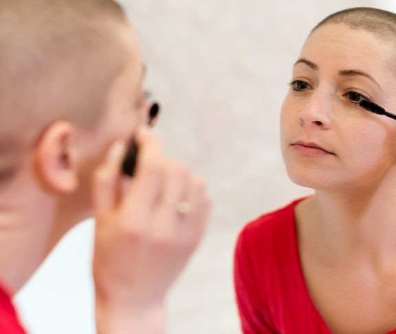 Young adult cancer survivor applying mascara