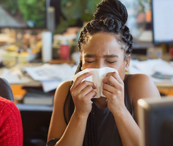 Another woman sneezing in an office