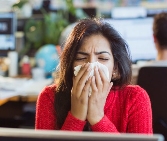 Woman sneezing in an office