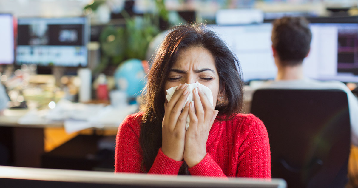 Woman sneezing in an office