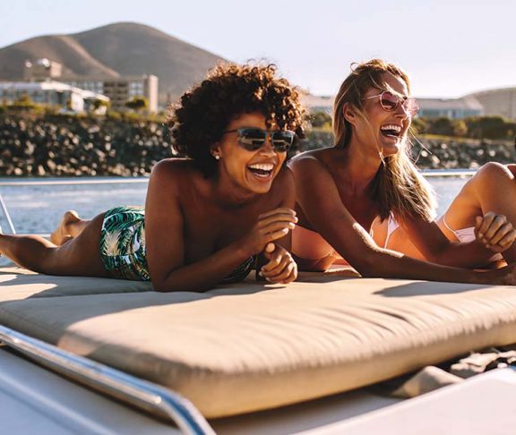 Three women laughing while sunbathing on a boat