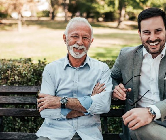 Two smiling men sitting on an outdoor bench