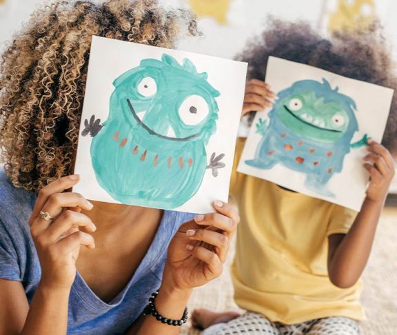 Mom and child holding drawings of cute monsters in front of their faces