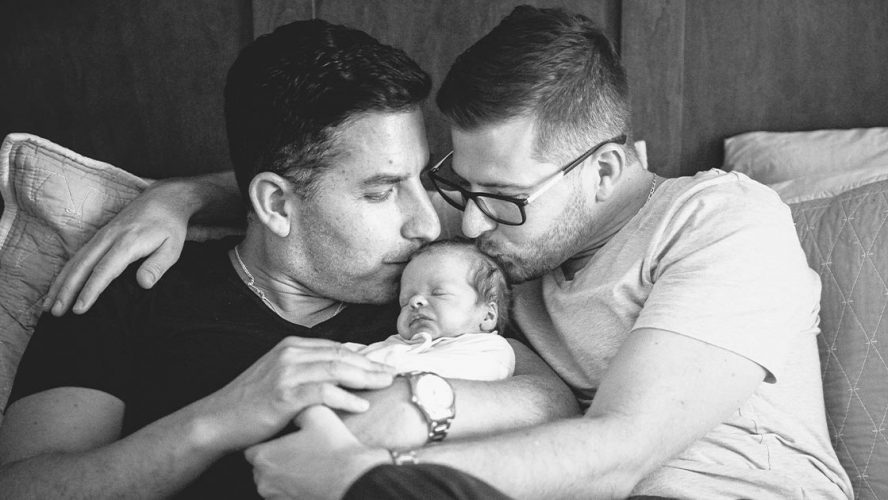 Two men kissing the head of their newborn child