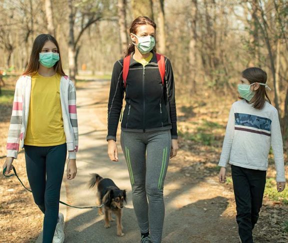 Mother and two daughters wearing medical face masks and hiking with their dog