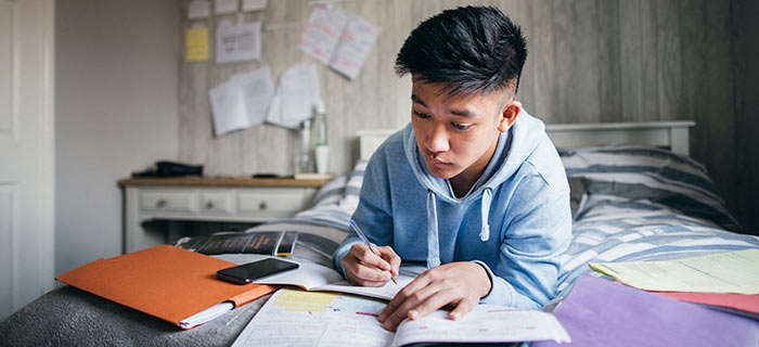 Male university student studying on his dorm room bed