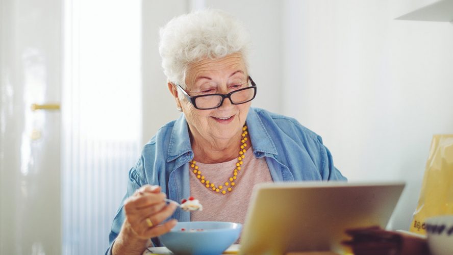 Elderly woman reading while eating a meal in her kitchen