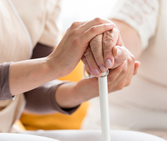 A person holds a white cane, while a health care professional places their hands around theirs.