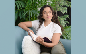 A woman sits comfortably on a blue couch and holds an open book in her hand.
