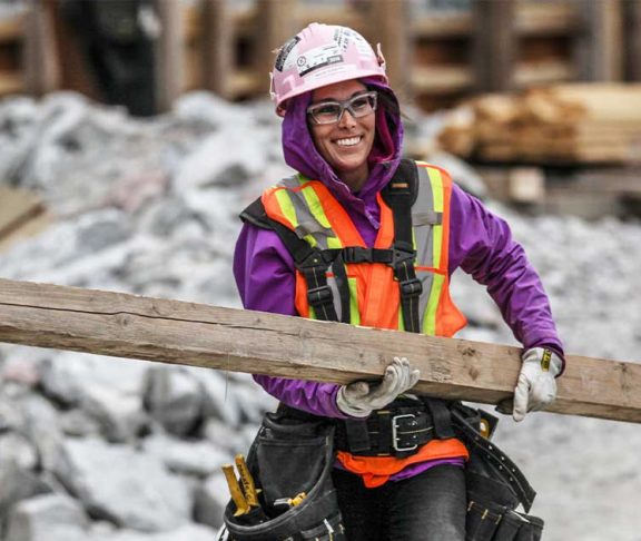 Female construction worker carrying beam through worksite