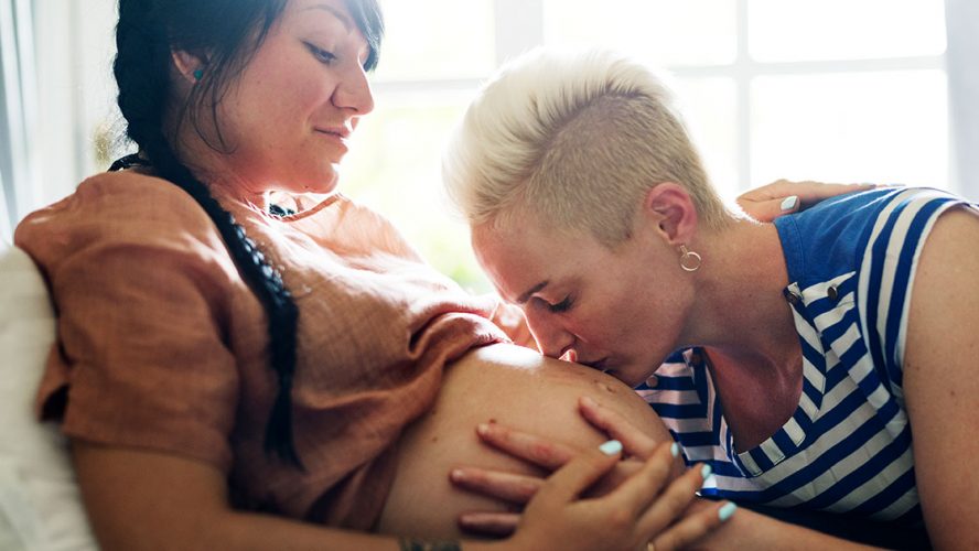 Two queer partners, one kissing the other's pregnant belly
