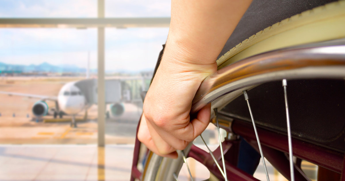 Close-up of a person's hand on their wheelchair wheel while looking at an airplane
