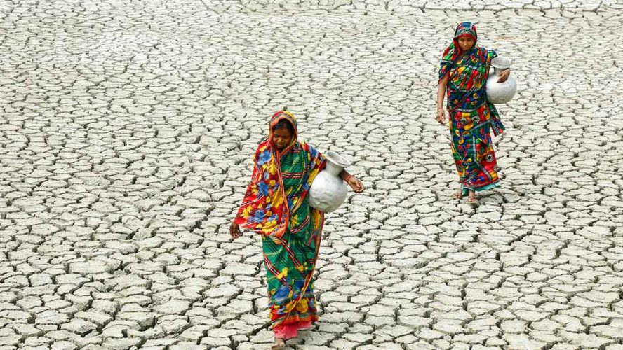 Women carrying jugs of water across dry land