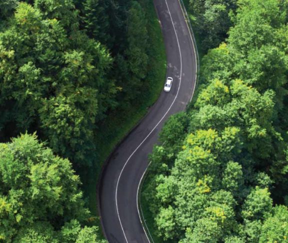 Aerial photo of a car driving down a road surrounded by forest