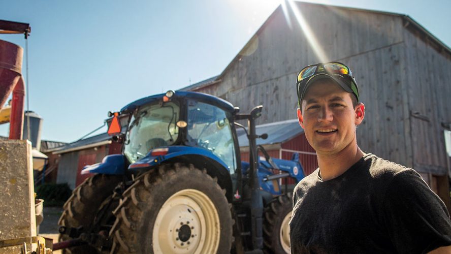 Andrew Campbell on a farm in front of a tractor and barn