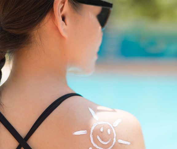 Teen at pool in bathing suit with a smiling sun of sunscreen on her shoulder