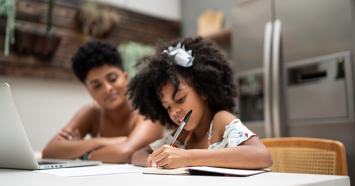 Young child writing in workbook with her mother