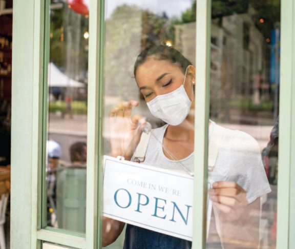 Businesswoman wearing a mask setting the OPEN sign of her restaurant