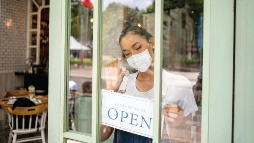 Businesswoman wearing a mask setting the OPEN sign of her restaurant