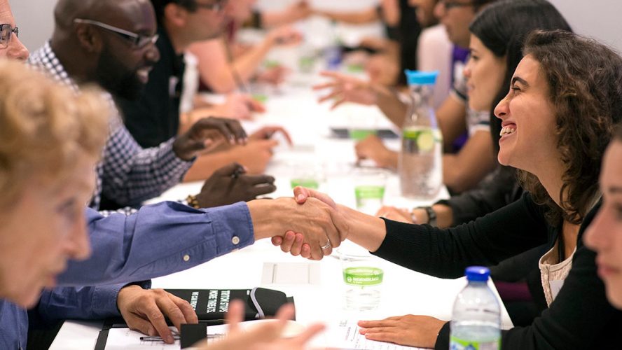 People smiling and shaking hands across a table at a professional event
