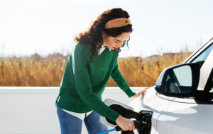 young woman in green sweater topping up EV vehicle