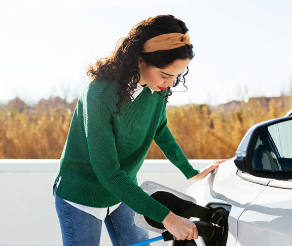 young woman in green sweater topping up EV vehicle