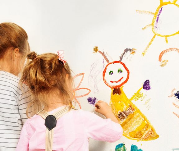 To små piger maler sol og figurer på hvid væg