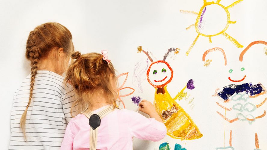 To små piger maler sol og figurer på hvid væg