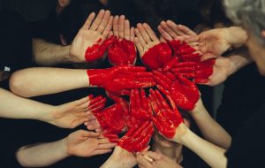 Flera händer tillsammans med röd färg som bildar ett hjärta för ideellt engagemang