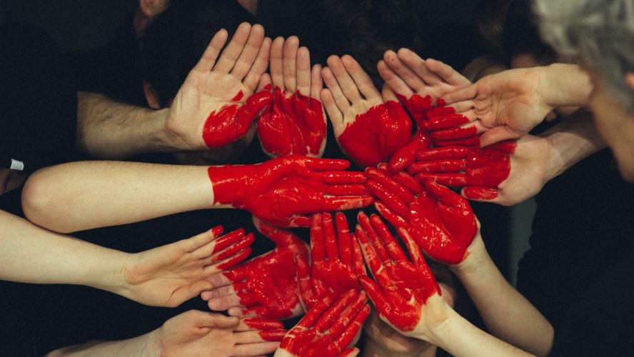 Flera händer tillsammans med röd färg som bildar ett hjärta för ideellt engagemang