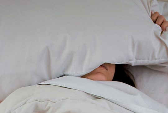 Kvinna som sover med kudden över huvudet.