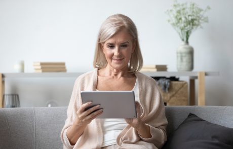 Portrait of pleasant middle aged woman sitting on cozy sofa, using tablet computer at home. Happy female retiree web surfing information, shopping in popular online store, reading electronic book.