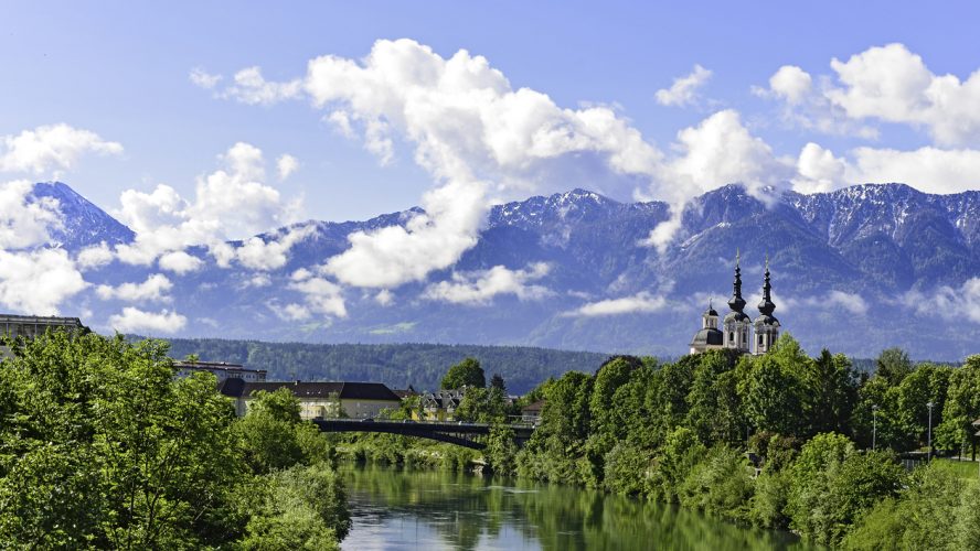 The Alps in Villach - mountain range in the clouds with a small chapel on the bank of the river