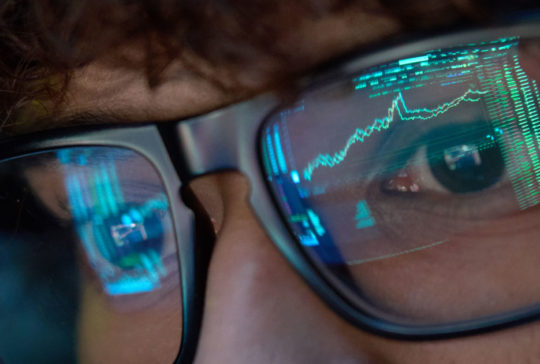 Young business man looking at trading charts reflecting in glasses, close up.