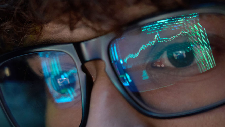 Young business man looking at trading charts reflecting in glasses, close up.