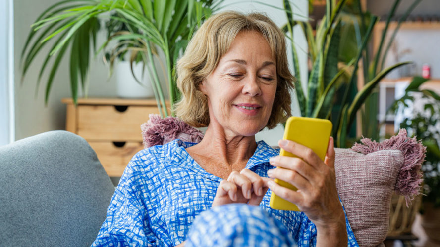 50-60 years old pretty female adult relaxing on the sofa and using smartphone