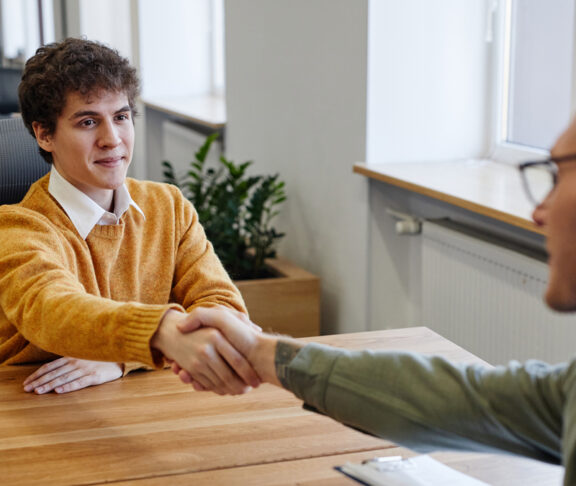 Portrait of smiling young man shaking hands with HR manager at job interview in office, copy space