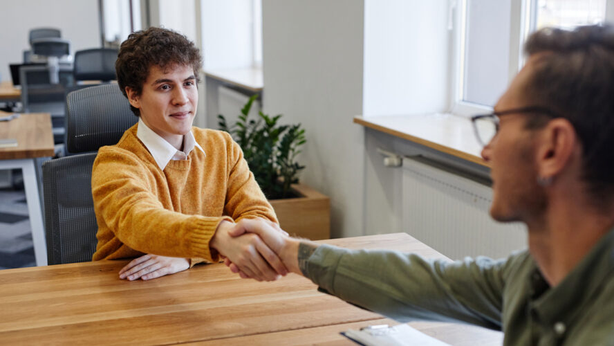 Portrait of smiling young man shaking hands with HR manager at job interview in office, copy space