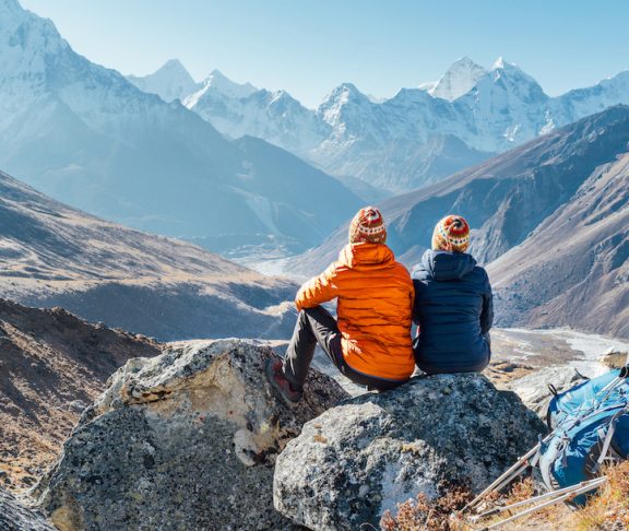 Couple resting on the Everest Base Camp trekking route near Dughla 4620m. Backpackers left Backpacks and trekking poles and enjoying valley view with Ama Dablam 6812m peak and Tobuche 6495m