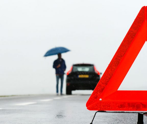 Mand med paraply og nedbrudt bil i regnvejr