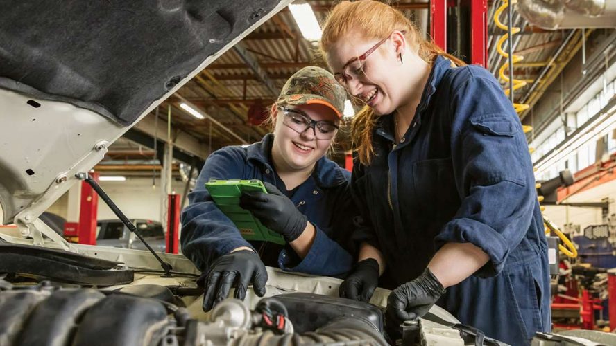 Two women working on an engine and smiling