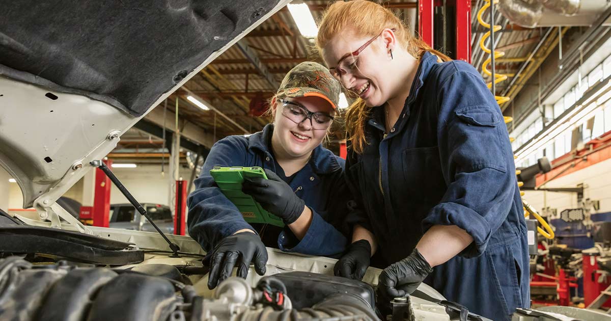 Two women working on an engine and smiling