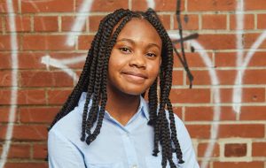 Young female Black mentee smiling in front of a brick wall